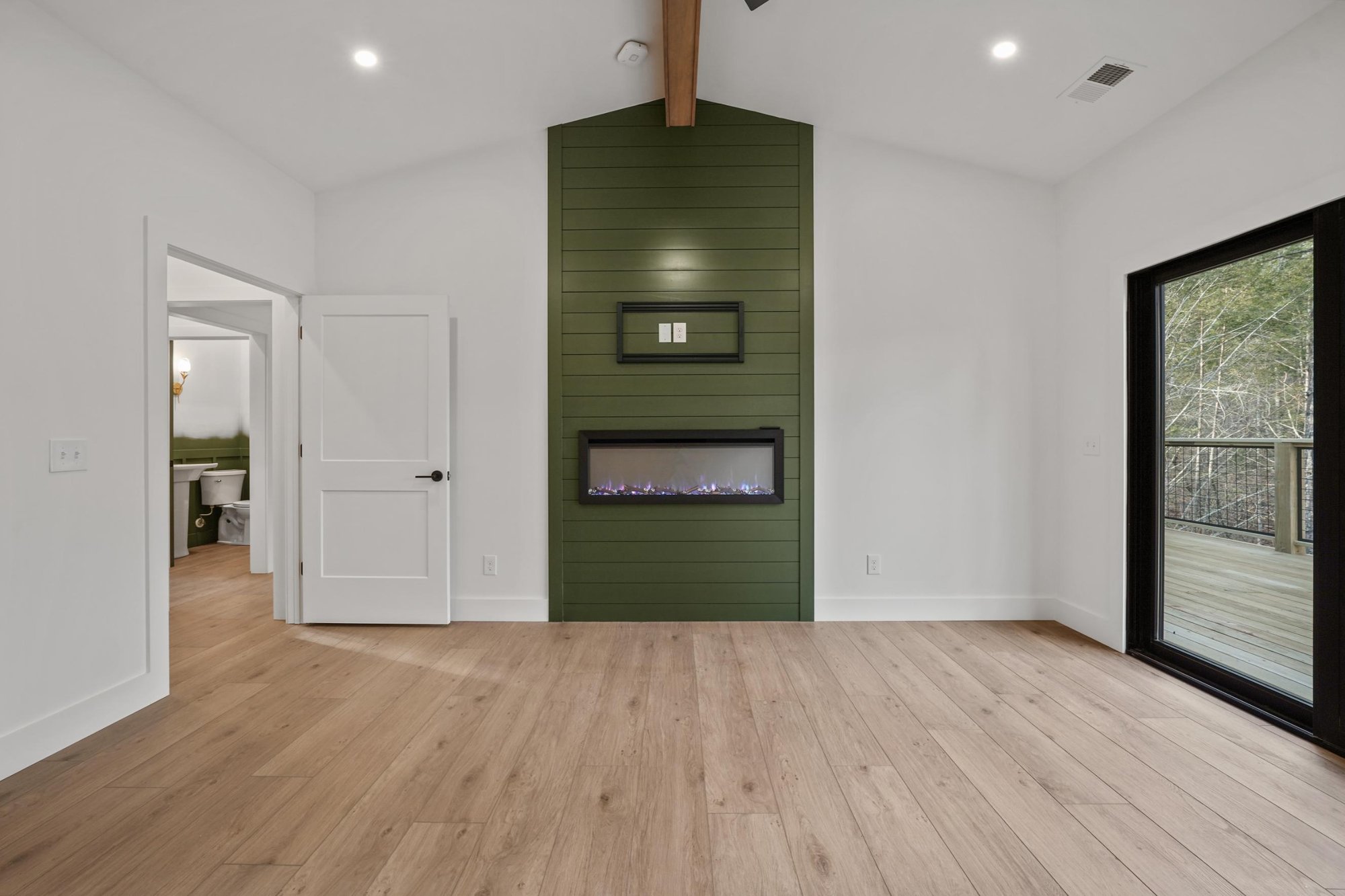 Electric fireplace and green paneling with exposed beams in the bedroom in Townsend, TN.