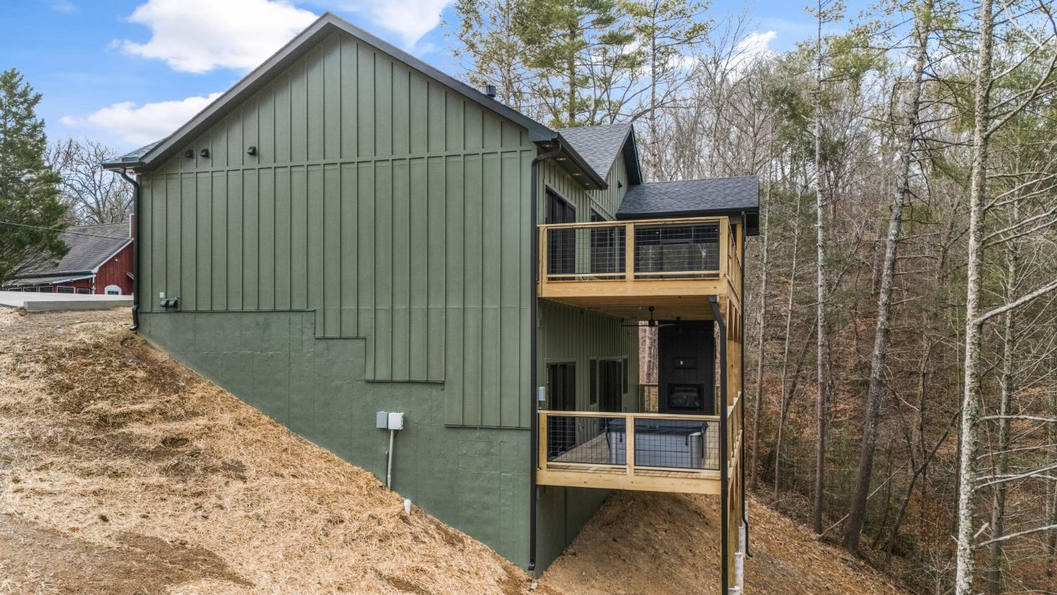 Side view of two-story green custom house on steep hill with double-decker deck and black roof with Hardie siding by Debuty Builders, Inc.