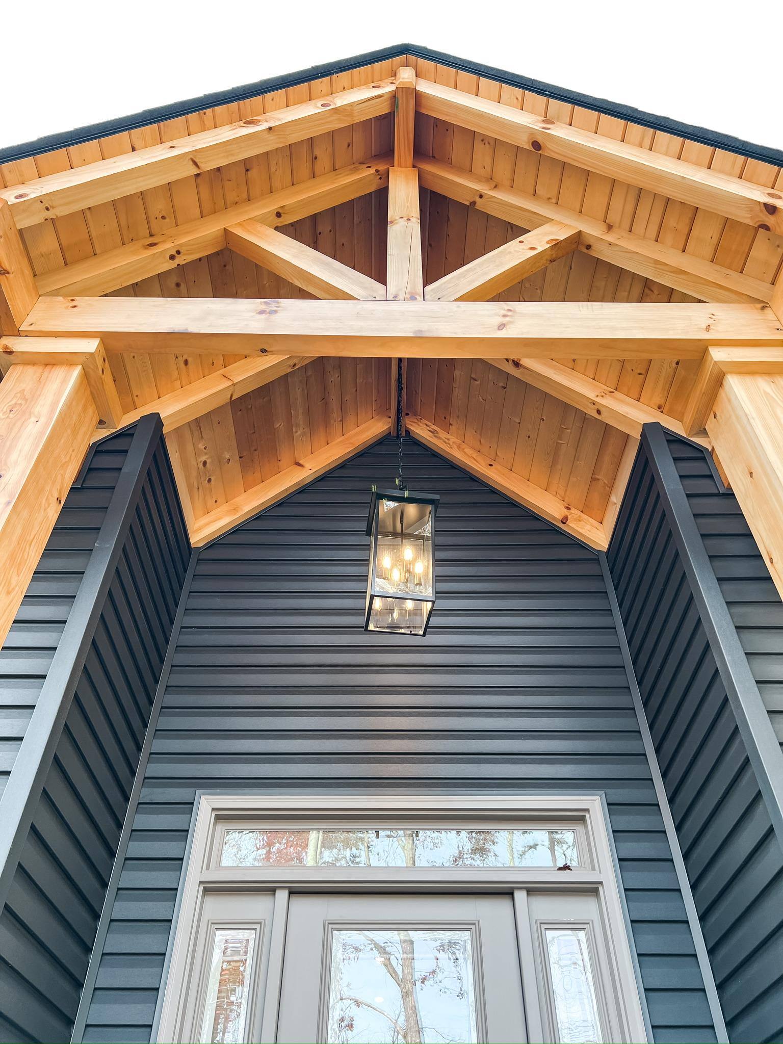 Close-up of a covered entryway with exposed timber beams and a modern hanging light in a custom home in Knoxville, TN by Debuty Builders, Inc. Close-up of a covered entryway with exposed timber beams and a modern hanging light in a custom home in Knoxville, TN by Debuty Builders, Inc.