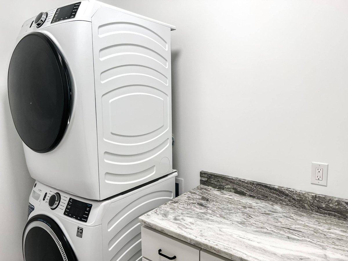 Stacked washer and dryer set next to a gray marble countertop in a modern laundry room, part of a custom home in Knoxville, TN by Debuty Builders, Inc.
