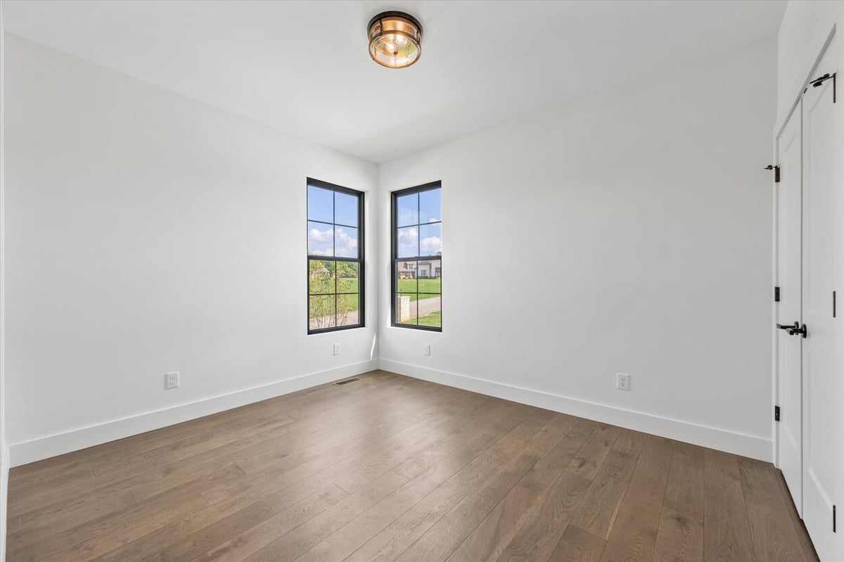 Bright secondary bedroom in a Louisville, TN custom home with corner windows and wood flooring