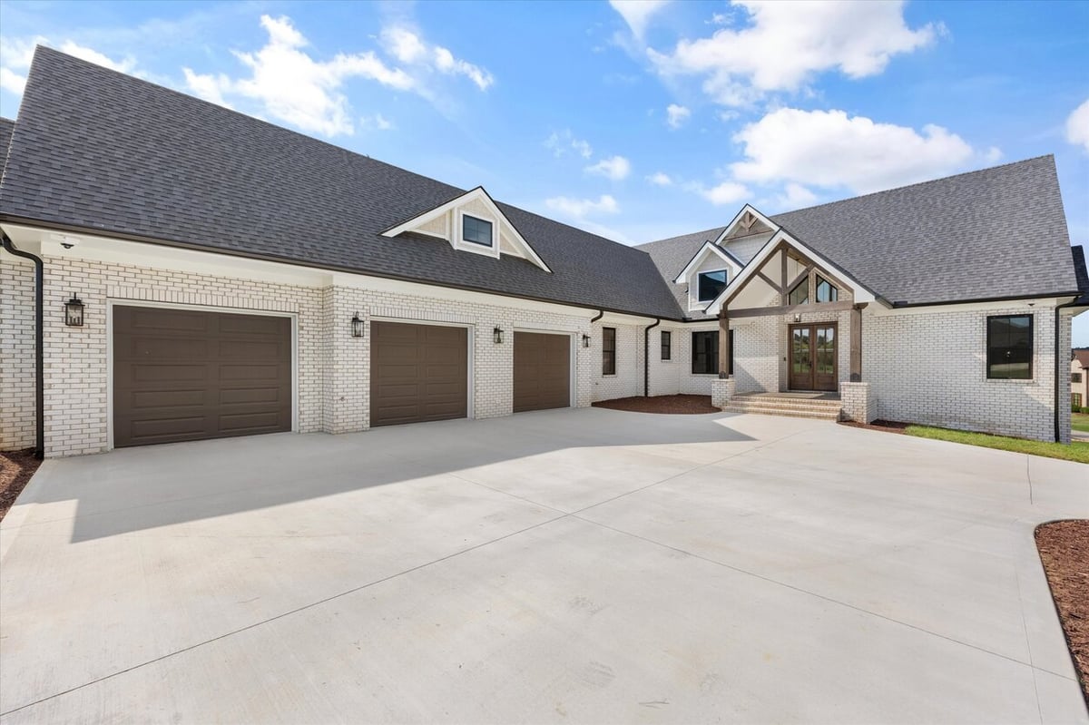 Exterior view of a Louisville, TN custom home featuring white brick, dark garage doors, and a wide concrete driveway