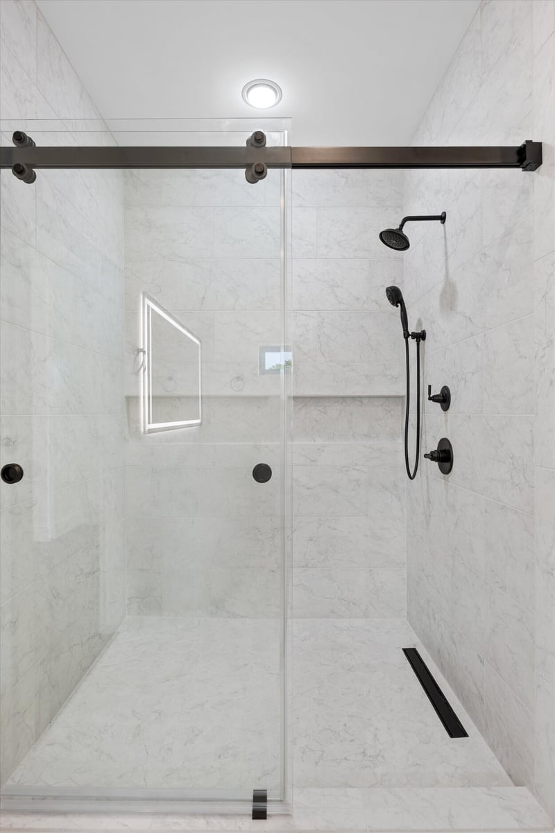 Walk-in shower with black fixtures and marble tile in a Louisville, TN custom home