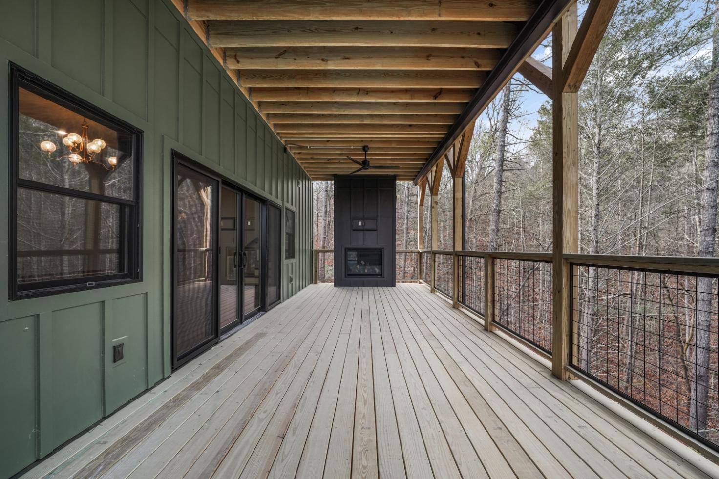 custom deck with built in fireplace, green walls, aluminum fence, and covered deck