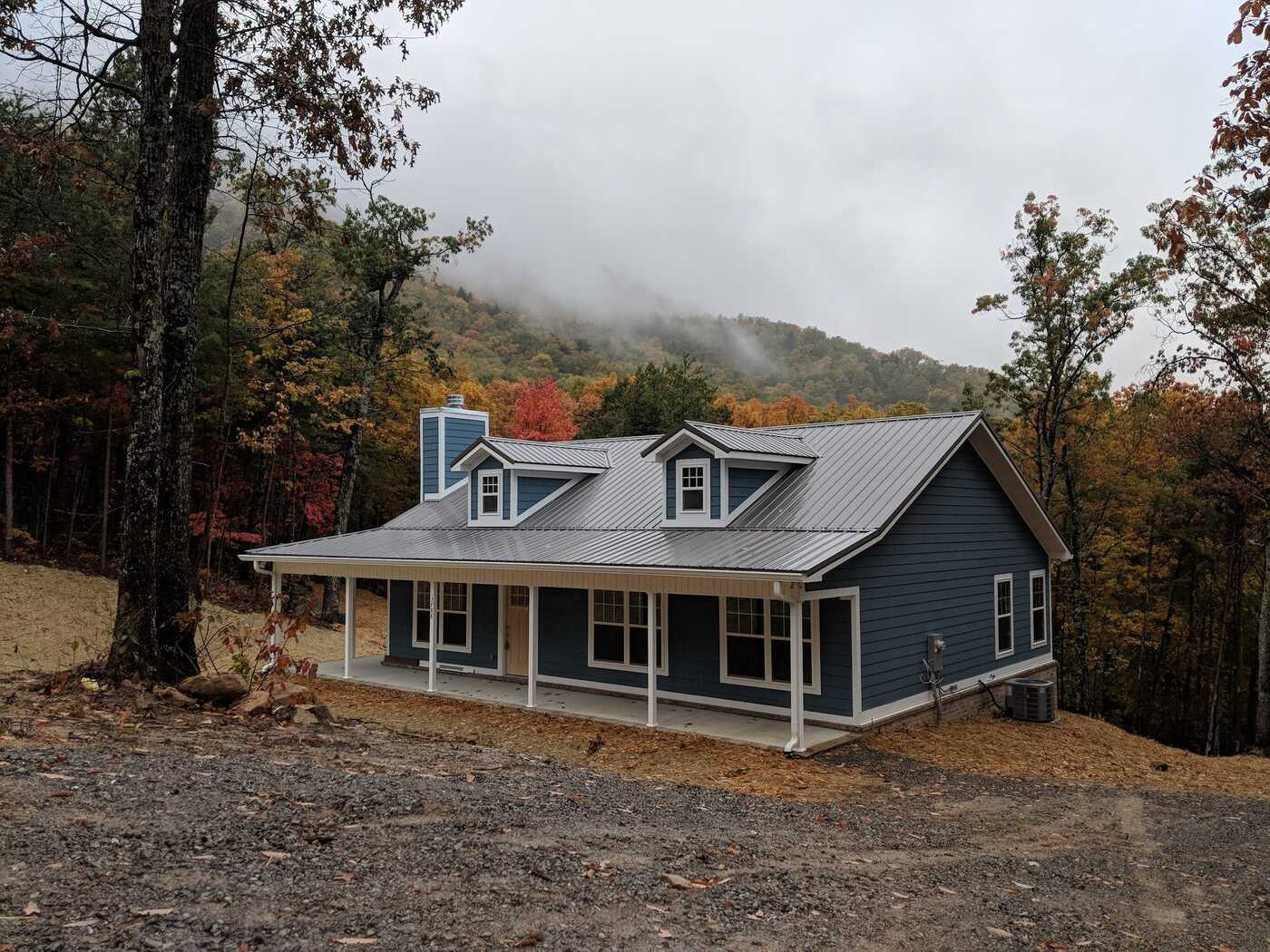 A blue custom-built cabin by Debuty Builders in Knoxville, TN, surrounded by autumn trees and misty mountains