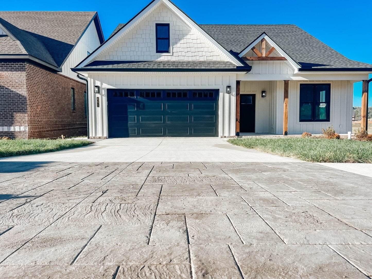 Custom home by Debuty Builders, Inc. in Maryville, TN, featuring a modern farmhouse design with a dark garage door, wood-accented columns, and a concrete driveway with stamped concrete detailing
